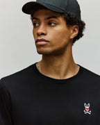 Person wearing a black t-shirt with a small logo on a plain background