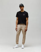 Person wearing a black t-shirt, beige pants, and white sneakers on a plain background