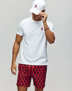 Person wearing a white t-shirt, red patterned shorts, and a white cap on a plain background