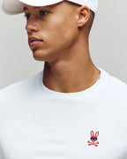 Person wearing a white t-shirt with a red logo on a plain background