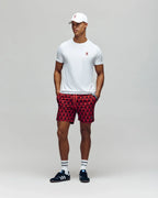 Man wearing a white t-shirt, red patterned shorts, and black sneakers on a gray background